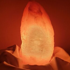 Glowing Himalayan salt lamp placed on draped fabric, creating a warm ambiance.