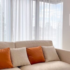 A couch with orange pillows sits by a window.